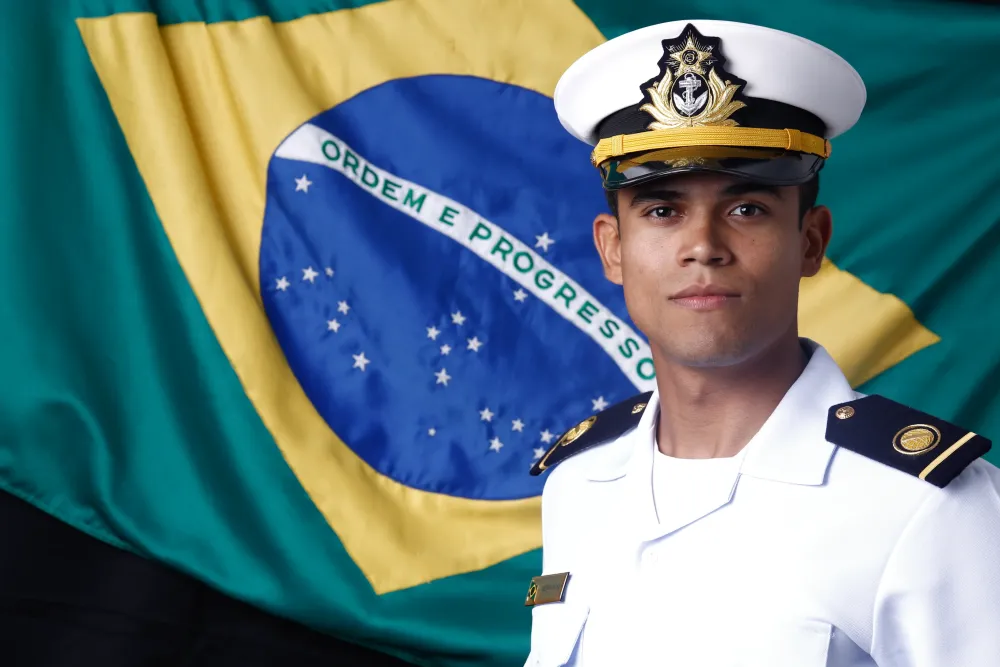 Matheus Renovato fardado diante da bandeira do Brasil, oficial do Corpo de Engenheiros da Marinha
